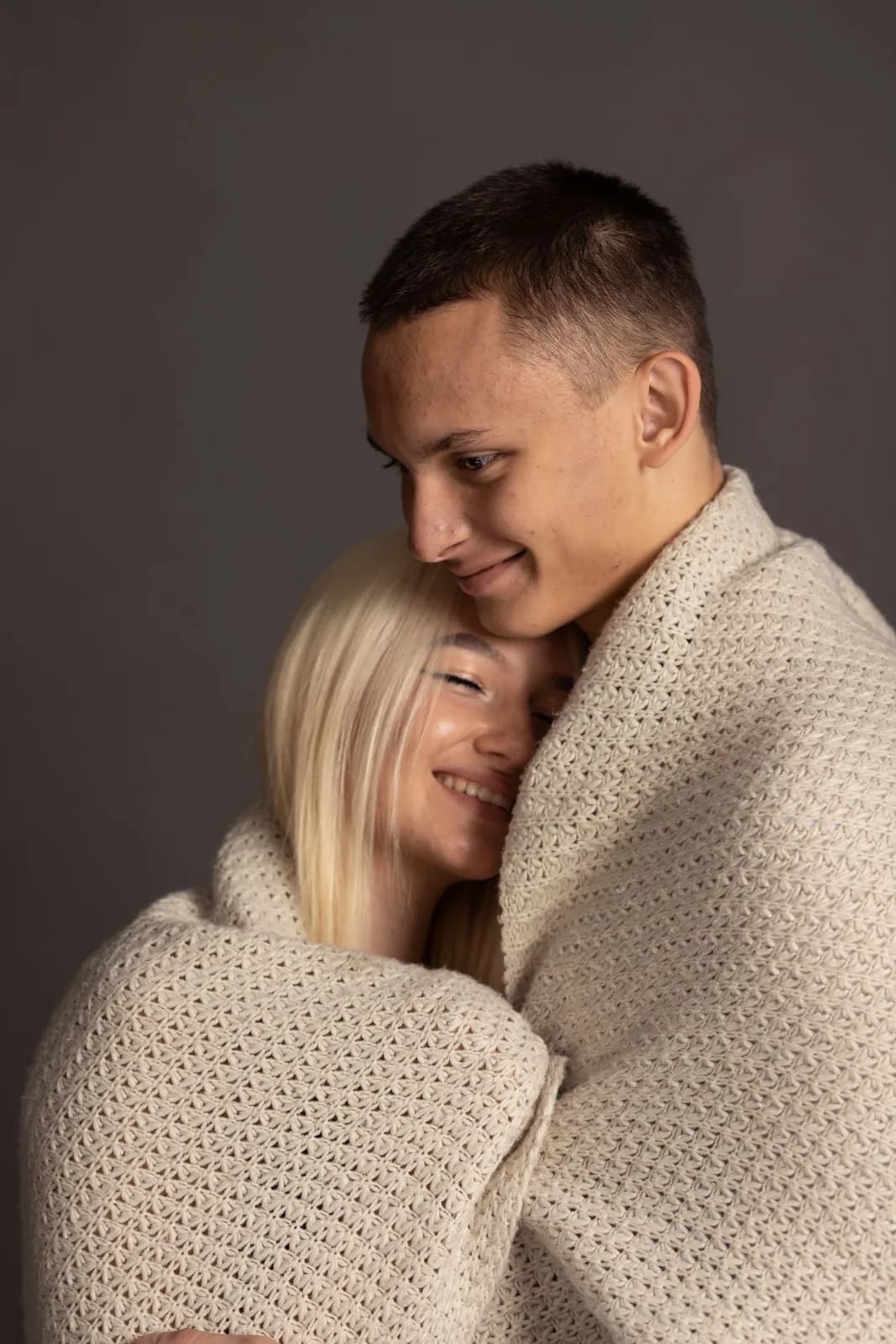 A couple wrapped together in a blanket, smiling